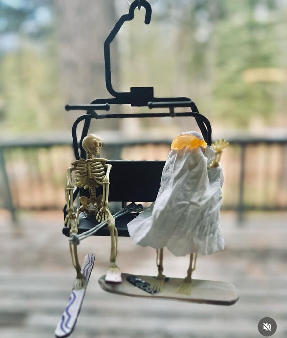 miniature skeletons in ski lift chair with skis and snowboards